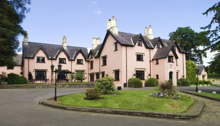 a blush pink 17th century converted manor house to hotel sits in the foreground of a scenic blue sky